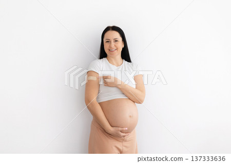 Pregnant woman pointing to vaccination bandage on arm while standing at home 137333636