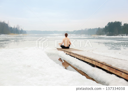 Shirtless man meditating in lotus position on a wooden dock over a frozen lake. Winter wellness concept with ice swimming and mindfulness in cold nature. High quality photo Shirtless man meditating in lotus position on a wooden dock over a frozen lake. Winter wellness concept with ice swimming and mindfulness in cold nature. High quality photo 137334038