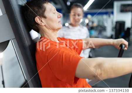 Senior woman training chest in gym with trainer Senior woman training chest in gym with trainer 137334130