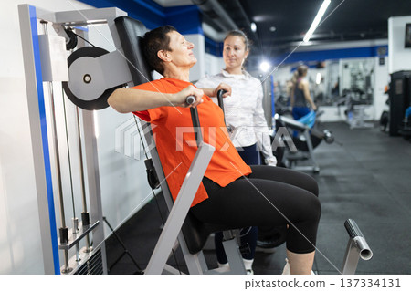 Mature woman exercising with personal trainer in gym Mature woman exercising with personal trainer in gym 137334131