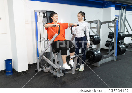 Mature woman training chest muscles with personal instructor 137334132