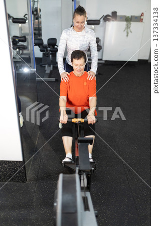 Personal trainer guiding senior woman on rowing machine workout Personal trainer guiding senior woman on rowing machine workout 137334138