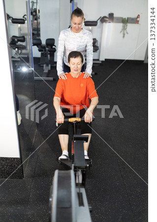 Senior woman exercising on rowing machine with personal trainer Senior woman exercising on rowing machine with personal trainer 137334144