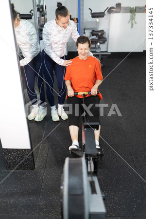 Senior woman training on rowing machine with instructor 137334145