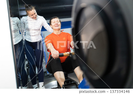 Senior woman training on rowing machine with personal coach 137334146