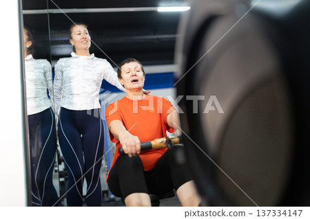 Senior woman exercising on rowing machine with trainer support 137334147