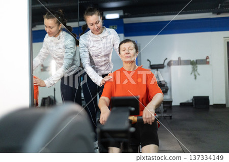 Senior woman training rowing machine with personal trainer 137334149