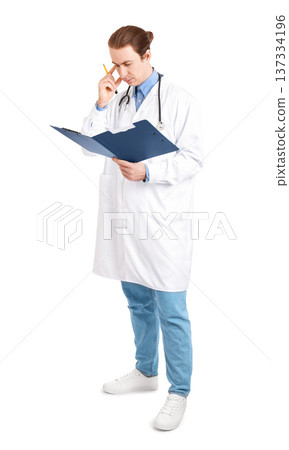 Young male doctor in a white coat studying a clipboard with a pensive expression. He holds a pencil to his temple, analyzing medical records. Isolated on white background. High quality photo 137334196