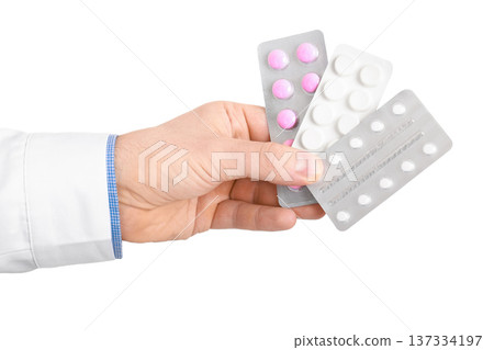 Doctor's hand holding three blister packs of different pills isolated on a white background. Concept of pharmacy, prescription, and healthcare treatment. High quality photo 137334197
