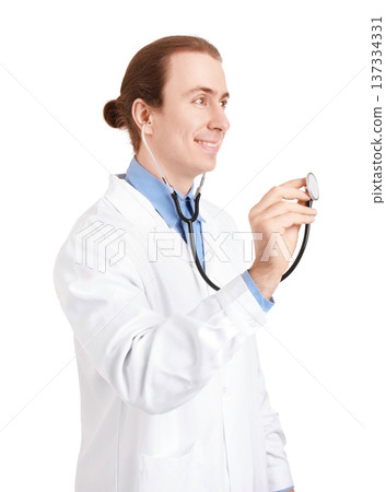 Side view of a smiling male doctor holding a stethoscope. Young medical professional with long hair in a white coat isolated on a white background, ready for an examination. High quality photo Side view of a smiling male doctor holding a stethoscope. Young medical professional with long hair in a white coat isolated on a white background, ready for an examination. High quality photo 137334331