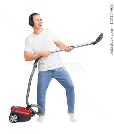 Young man in headphones playing vacuum cleaner like a guitar. Happy guy having fun while cleaning home isolated on white background. High quality photo 137334408