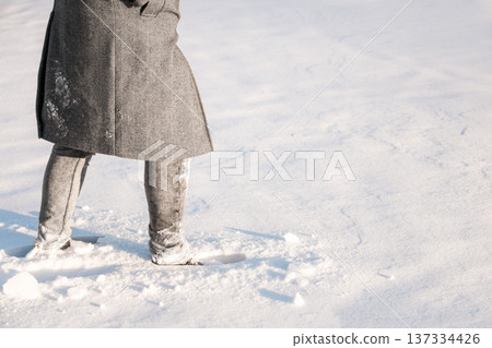 Legs of a person in a grey herringbone coat and jeans standing in deep snow on a sunny winter day. Concept of cold weather and winter fashion outdoors. High quality photo Legs of a person in a grey herringbone coat and jeans standing in deep snow on a sunny winter day. Concept of cold weather and winter fashion outdoors. High quality photo 137334426