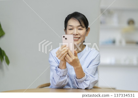 一位年近六十的女士看著她的智慧型手機螢幕，臉上帶著微笑。 137334531
