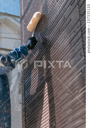 Female craftsman working at an exterior wall painting site (no face) Female craftsman working at an exterior wall painting site (no face) 137335110