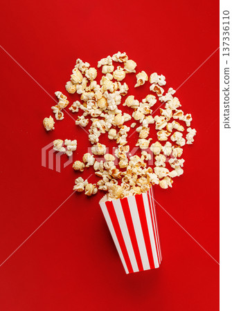 Popcorn exploding from striped bucket on red background. Creative cinema snack concept. 137336110
