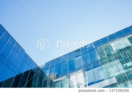 Modern office building corner made of reflective glass. Commercial property exterior. Reflection of financial district skyscrapers, clear blue sky background. Modern office building corner made of reflective glass. Commercial property exterior. Reflection of financial district skyscrapers, clear blue sky background. 137336200