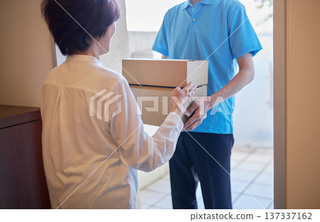 一名女子正在接收包裹，一名送貨員正在送貨。 137337162
