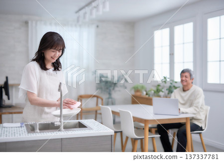 一對六十多歲的男女一邊在廚房擦碗碟，一邊微笑交談。 137337781