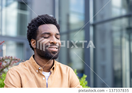 Young man standing outdoors with closed eyes and a serene smile, experiencing a moment of calm and mindfulness, finding relaxation and inner peace in the open air 137337835
