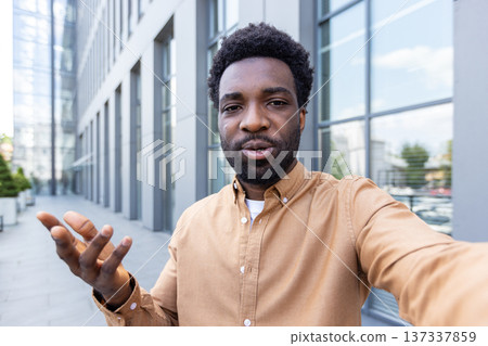 African american businessman talking during a virtual meeting, gesturing with his hand and communicating remotely against a modern urban building backdrop African american businessman talking during a virtual meeting, gesturing with his hand and communicating remotely against a modern urban building backdrop 137337859