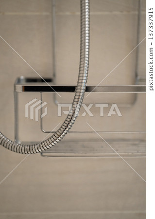 Chrome shower hose hanging next to a sleek metal bathroom shelf with a contemporary design, illustrating modern plumbing and hygiene in a home shower 137337915