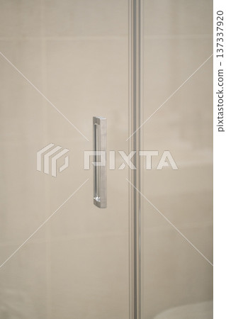 Chrome handle on a transparent glass shower door in a contemporary bathroom, reflecting ambient light from the interior, focusing on modern design and cleanliness 137337920