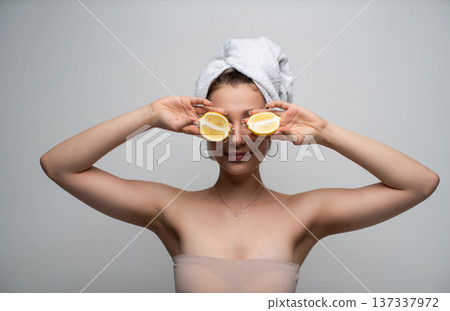 Woman with towel holding lemon halves near eyes symbolizing natural skincare, freshness and vitamin C wellness routine for healthy beauty and spa treatment Woman with towel holding lemon halves near eyes symbolizing natural skincare, freshness and vitamin C wellness routine for healthy beauty and spa treatment 137337972