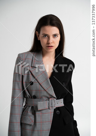 Young woman posing in studio wearing a belted two-tone blazer—black on one side, grey plaid on the other—modern, chic, and confidently stylish portrait Young woman posing in studio wearing a belted two-tone blazer—black on one side, grey plaid on the other—modern, chic, and confidently stylish portrait 137337996