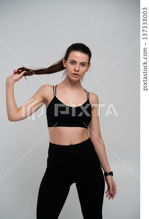 Fit woman in black sportswear holding hair, projecting confidence, strength, and an active lifestyle, embodying fitness and self-care in a studio setting Fit woman in black sportswear holding hair, projecting confidence, strength, and an active lifestyle, embodying fitness and self-care in a studio setting 137338003