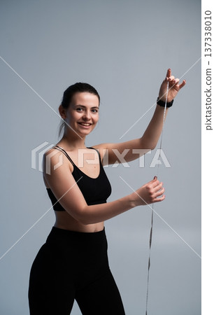 Young woman smiling, holding a measuring tape and celebrating progress towards fitness goals, managing weight loss journey and body transformation on a studio background Young woman smiling, holding a measuring tape and celebrating progress towards fitness goals, managing weight loss journey and body transformation on a studio background 137338010