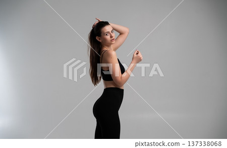 Attractive young woman with dark hair in activewear training, embodying fitness and health concepts, preparing for workout in studio on gray background Attractive young woman with dark hair in activewear training, embodying fitness and health concepts, preparing for workout in studio on gray background 137338068