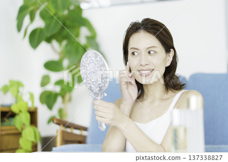 一位中年日本女性在客廳的鏡子前看著自己，擔憂自己的皮膚狀況。 137338827