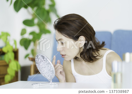 A middle-aged Japanese woman looking in the mirror in the living room and worrying about her skin condition A middle-aged Japanese woman looking in the mirror in the living room and worrying about her skin condition 137338987