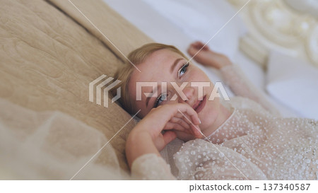 Bride relaxing on bed, white wedding gown draping softly, capturing peaceful moments before exchanging vows Bride relaxing on bed, white wedding gown draping softly, capturing peaceful moments before exchanging vows 137340587