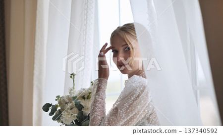 Elegant blonde bride clutching white wedding bouquet, radiating happiness during wedding day preparations Elegant blonde bride clutching white wedding bouquet, radiating happiness during wedding day preparations 137340592
