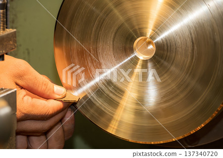 Manual surface finishing of a brass component on a lathe machine using progressive abrasive sandpaper for high-quality polishing. Manual surface finishing of a brass component on a lathe machine using progressive abrasive sandpaper for high-quality polishing. 137340720