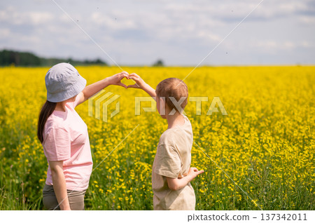 Mother and son making a heart shape with hands while standing in blooming rapeseed field on a sunny day Mother and son making a heart shape with hands while standing in blooming rapeseed field on a sunny day 137342011