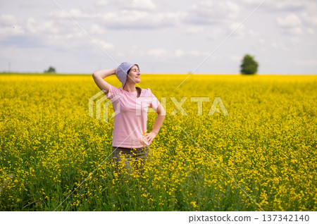 Woman in bucket hat raising arms up, enjoying a warm summer day in a blooming yellow rapeseed field Woman in bucket hat raising arms up, enjoying a warm summer day in a blooming yellow rapeseed field 137342140