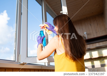 Woman cleaning window seen from behind in bright room Woman cleaning window seen from behind in bright room 137342197