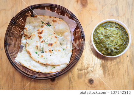 Indian Palak Paneer Curry With Garlic Naan Bread on Wooden Table Indian Palak Paneer Curry With Garlic Naan Bread on Wooden Table 137342513