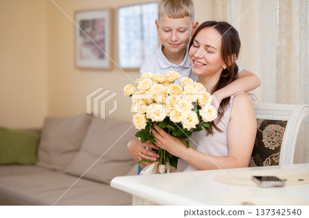Teenage boy hugs and kisses mother while giving yellow roses bouquet for Mother's Day 137342540