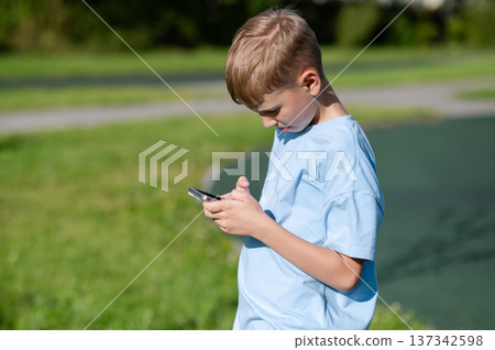 Teen boy looking at smartphone in park Teen boy looking at smartphone in park 137342598