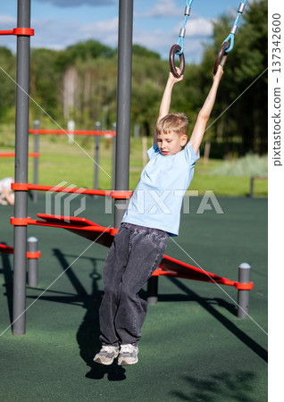 Blond teen boy on gymnastic rings outdoors 137342600