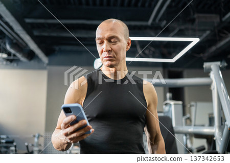Athletic man checking smartphone during gym workout Athletic man checking smartphone during gym workout 137342653
