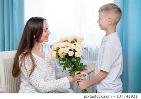 Teenage boy hugging mother and giving bouquet of yellow roses for Mother's Day at home Teenage boy hugging mother and giving bouquet of yellow roses for Mother's Day at home 137342921
