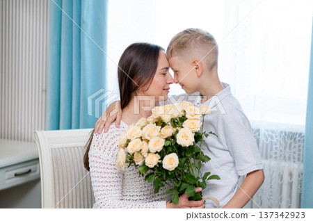 Teenage boy hugging mother and giving bouquet of yellow roses for Mother's Day at home Teenage boy hugging mother and giving bouquet of yellow roses for Mother's Day at home 137342923