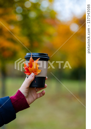 Woman holding paper cup with hot drink in autumn forest with colorful fall foliage Woman holding paper cup with hot drink in autumn forest with colorful fall foliage 137343086