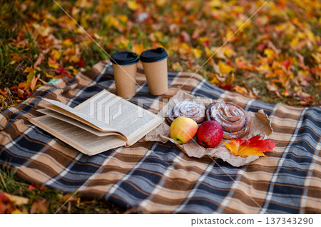 Cozy autumn picnic scene with plaid, two paper cups of hot drinks, pastries, apples and a book 137343290