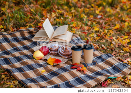Cozy autumn picnic scene with plaid, two paper cups of hot drinks, pastries, apples and a book 137343294