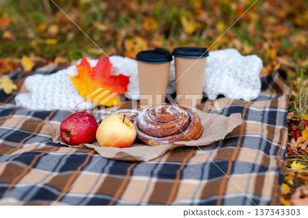 Cozy autumn picnic scene with plaid, knitted sweater, two paper cups of hot drinks, pastries, apples and falling maple leaves Cozy autumn picnic scene with plaid, knitted sweater, two paper cups of hot drinks, pastries, apples and falling maple leaves 137343303